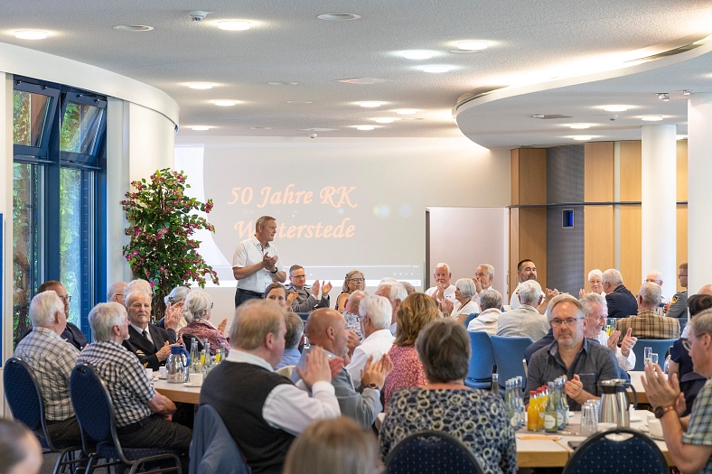 Feierliche Veranstaltung mit sitzenden Personen, Präsentation und Pflanzendekoration.