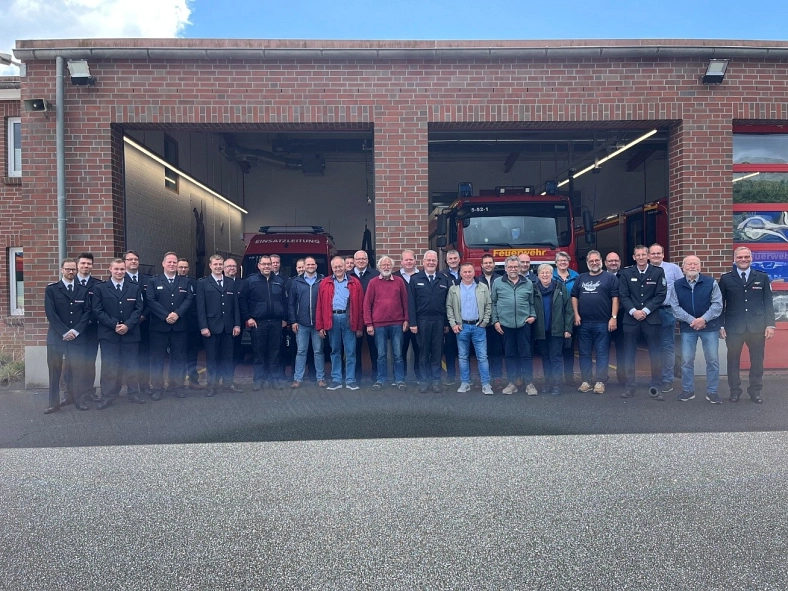 Gruppe von Feuerwehrleuten und Ehrengästen vor einem Feuerwehrfahrzeug in einer Ziegelgarage.
