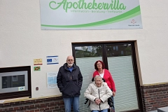 Drei Personen vor dem Gebäude der Apothekervilla mit dem Schriftzug „Information · Beratung · Treffpunkt“.