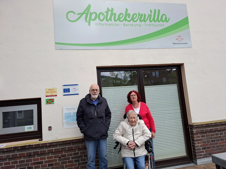 Drei Personen vor dem Gebäude der Apothekervilla mit dem Schriftzug „Information · Beratung · Treffpunkt“.