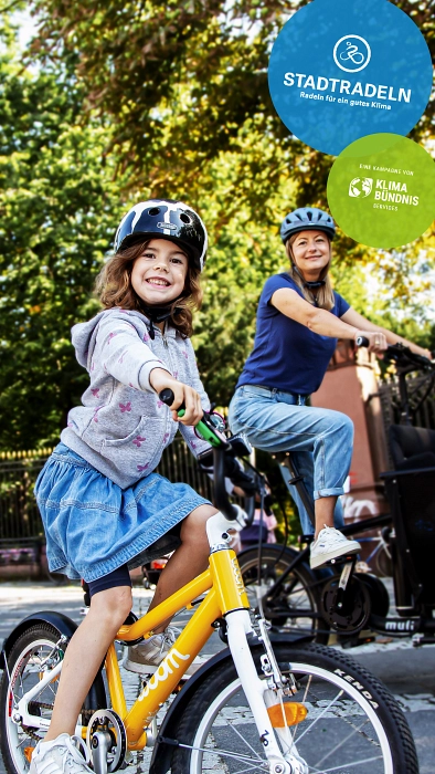 2026-06_Stadtradeln 2026 Kind und erwachsene Frau fahren Fahrräder, begleitet von einem "Stadtradeln"-Poster. © Klima Bündnis Services