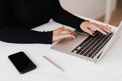 Person mit schwarzen Nägeln tippt auf einem Laptop neben Smartphone und Stift auf weißem Tisch.
pexels_karolina_grabowska_4467735.jpg