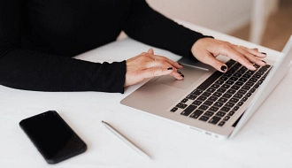 Person mit schwarzen Nägeln tippt auf einem Laptop neben Smartphone und Stift auf weißem Tisch.
pexels_karolina_grabowska_4467735.jpg